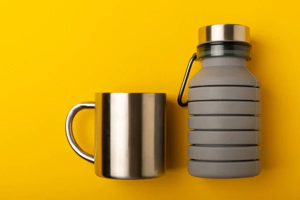 Travel bottle and mug for water. Flask and metal mug. Travel set on a yellow background. View from above. copy space.Place for text. MOCKUP