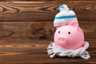 Tasarruf kavramı. Domuz kumbarası ve sarı dokuma üzerine para. Sıcak bir kış şapkası takmış, sıcağı kurtaran bir kumbara. Isıtma tasarrufu kavramı. Mesaj için yer. Boşluğu kopyala