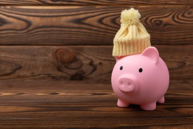 Tasarruf kavramı. Domuz kumbarası ve sarı dokuma üzerine para. Sıcak bir kış şapkası takmış, sıcağı kurtaran bir kumbara. Isıtma tasarrufu kavramı. Mesaj için yer. Boşluğu kopyala