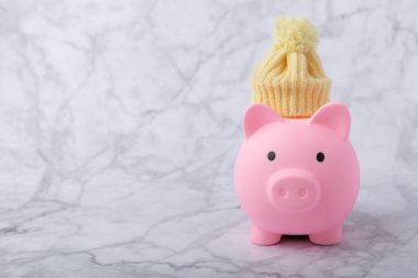 Tasarruf kavramı. Domuz kumbarası ve sarı dokuma üzerine para. Sıcak bir kış şapkası takmış, sıcağı kurtaran bir kumbara. Isıtma tasarrufu kavramı. Mesaj için yer. Boşluğu kopyala