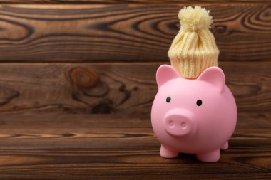 Tasarruf kavramı. Domuz kumbarası ve sarı dokuma üzerine para. Sıcak bir kış şapkası takmış, sıcağı kurtaran bir kumbara. Isıtma tasarrufu kavramı. Mesaj için yer. Boşluğu kopyala