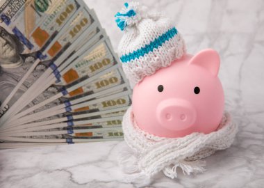 Tasarruf kavramı. Domuz kumbarası ve beyaz mermer desenli arka planda para. Seni sıcak tutan, kışlık şapkalı bir kumbara. Isı tasarrufu kavramı. Mesaj için yer. Boşluğu kopyala