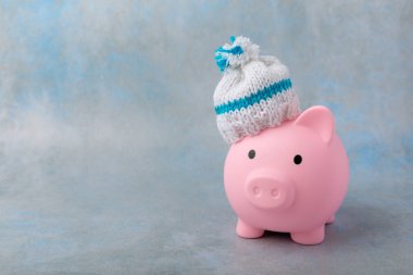 Tasarruf kavramı. Domuz kumbarası ve sarı dokuma üzerine para. Sıcak bir kış şapkası takmış, sıcağı kurtaran bir kumbara. Isıtma tasarrufu kavramı. Mesaj için yer. Boşluğu kopyala