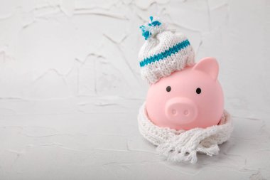 Tasarruf kavramı. Domuz kumbarası ve sarı dokuma üzerine para. Sıcak bir kış şapkası takmış, sıcağı kurtaran bir kumbara. Isıtma tasarrufu kavramı. Mesaj için yer. Boşluğu kopyala