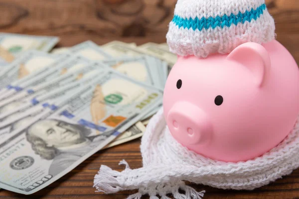 Savings concept. Piggy bank and money on brown texture background. A piggy bank in a warm winter hat that keeps you warm. Heat saving concept. Place for text. copy space
