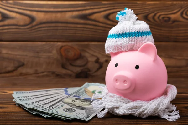 Savings concept. Piggy bank and money on brown texture background. A piggy bank in a warm winter hat that keeps you warm. Heat saving concept. Place for text. copy space