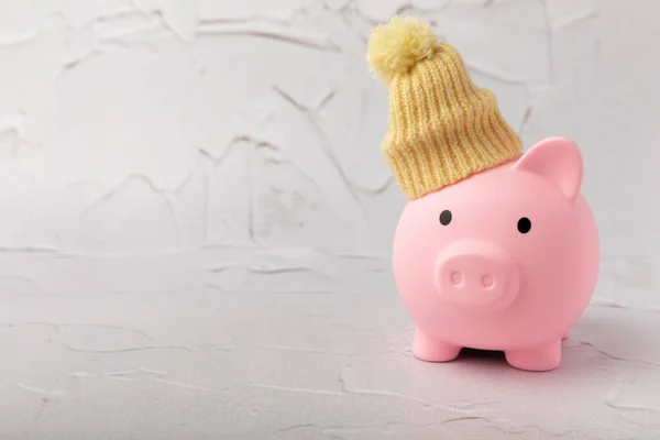 Savings concept. Piggy bank and money on a yellow textural background. A piggy bank in a warm winter hat that saves heat. The concept of saving heating. Place for text. copy space