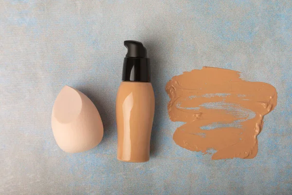 Image of liquid foundation bb cream or concealer.Foundation cream and beauty blender on blue marble background.
