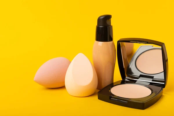 Makeup accessories,beauty blender,powder and foundation on a yellow textural background.beauty and fashion. Beauty concept