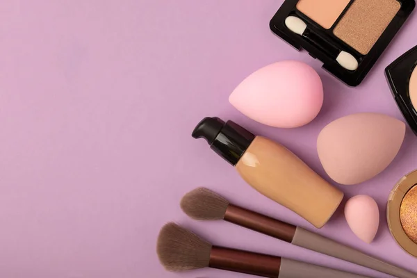 Makeup accessories, beauty blender and makeup brushes. Powder, foundation, eye shadow and blush on a lilac texture background. beauty and fashion. Beauty concept