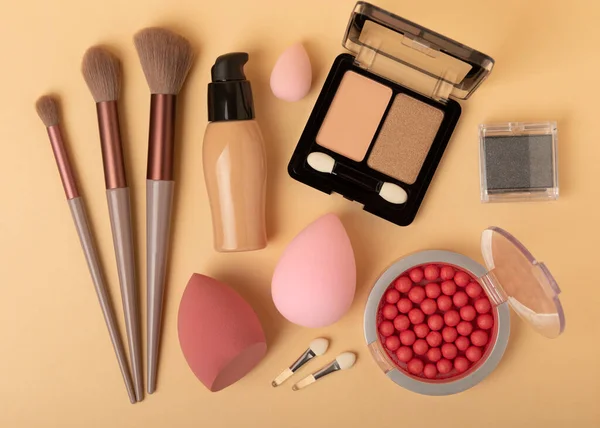 Makeup accessories,beauty blender and makeup brushes.Powder,foundation,eye shadows and blush on a beige textured background.