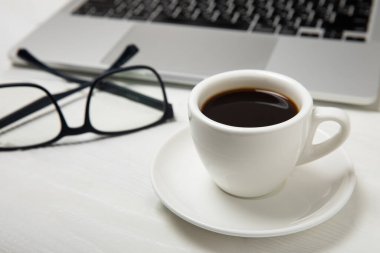 Ofis masasının en üst görüntüsü. Dizüstü bilgisayarı, bardakları ve kahve fincanı olan çalışma alanı siyah arka planda..