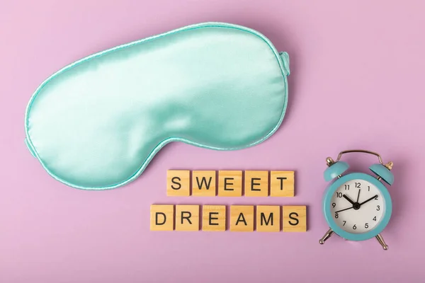 Sleeping masks, an alarm clock and the inscription SWEET DREAMS on a lilac background. The concept of relaxation and sleep quality. Sweet dreams and good night. Insomnia. Relaxation. Place to copy.