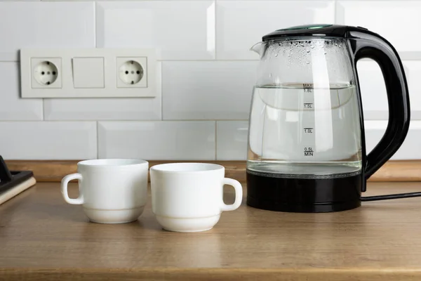 A man makes tea using boiling water from an electric kettle in the kitchen at home. It's time to have breakfast and drink tea. Modern electric kettle on a wooden table. Kettle for boiling water.