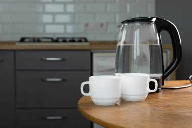 A man makes tea using boiling water from an electric kettle in the kitchen at home. It's time to have breakfast and drink tea. Modern electric kettle on a wooden table. Kettle for boiling water.