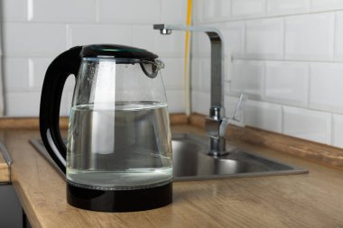 Modern electric transparent kettle on a wooden table in the kitchen.Kettle for boiling water and making tea.Home appliances for making hot drinks.Space for copy.Place for text.