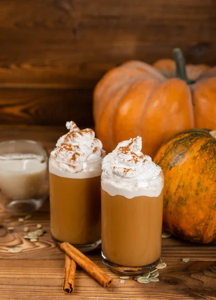 Pumpkin spice latte in glass mug with cinnamon, nutmeg, pumpkin seeds and whipped cream on brown texture wood. A glass of autumn coffee with pumpkin. A warming drink. Autumn concept.