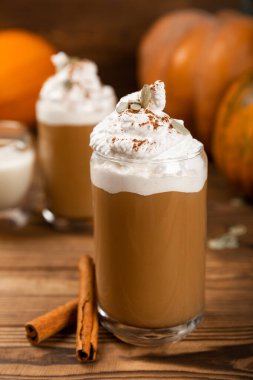 Cam bardakta balkabağı aromalı latte, tarçın, hindistan cevizi, kabağı çekirdeği ve kahverengi desenli ahşap krema. Balkabaklı bir bardak sonbahar kahvesi. Sıcak bir içecek. Sonbahar konsepti.