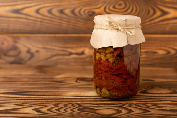 Dried tomatoes in a jar with spices and herbs. Autumn seasonal pickled vegetables. Autumn home canning products. Side view. Composition on a wooden table.