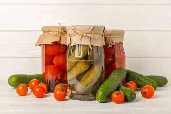 Jars with pickled vegetables. Pickled food.Jars of pickled vegetables: cucumbers and tomatoes on a rustic wooden background. Pickled and canned foods.