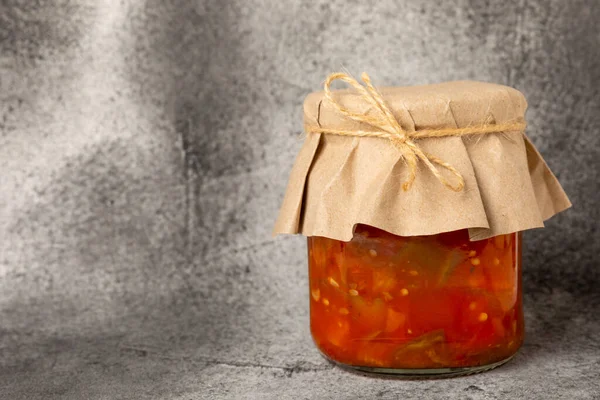 Glass jar of delicious canned lecho on a black textured background. side view. Salad in a jar.