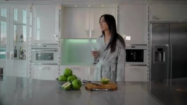 Muhteşem beyaz bir mutfakta genç ve güzel bir kız şeffaf bir bardaktan temiz su içiyor..