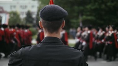 Bir askeri birlik, bereli bir paraşütçünün arka planına doğru ilerliyor.