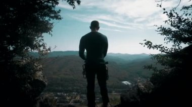 Tırmanış takımları içinde bir uçurumun kenarında durur ve bir kask takar. Panorama 4K.