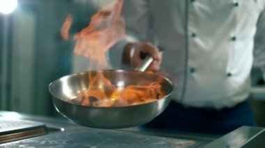 Beyaz önlüklü adam mutfaktaki tavada et pişiriyor.