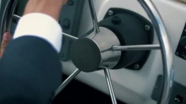Klasik takım elbiseli başarılı bir girişimci, yolculukta yatının direksiyonunu kontrol eder. Yakın plan.