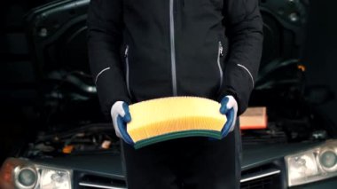 Tamirci, bir otomobil benzin istasyonunda bakım için yeni bir temiz araba hava filtresi tutuyor..