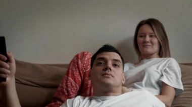 Genç ve mutlu bir aile yeni evlerinde kanepede yüzlerinde tebessümle televizyon seyrediyor.