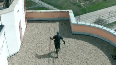 Extreme in the gear of industrial mountaineering runs up and jumps from the roof of a high multi-storey skyscraper on a rope.