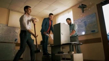 Three men in office clothes are trying to open a heavy iron safe with autogen and a big sledgehammer