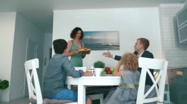 Genç ve mutlu bir aile kahvaltıdan önce masaya oturur.