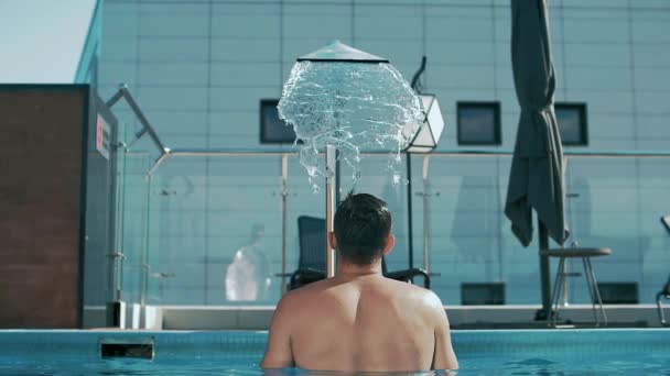一个年轻人站在一家豪华酒店的淋雨淋浴间的游泳池里 慢动作 — 图库视频影像
