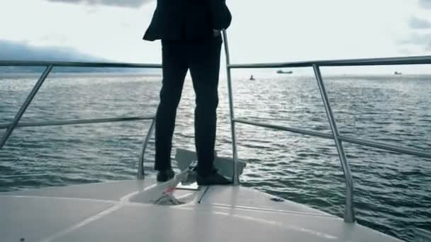 穿着燕尾服的富有的成功人士站在他的大游艇的鼻梁上 横渡大海 遥望远方 — 图库视频影像