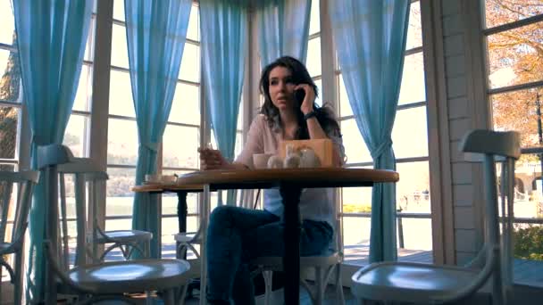 漂亮的小女孩坐在咖啡店的桌子旁 一边打电话一边笑 — 图库视频影像