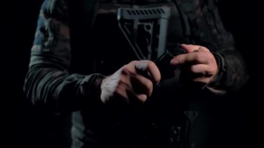 Siyah arka planda kamuflaj gömlekli bir adam AK dergisine fişek yüklüyor.