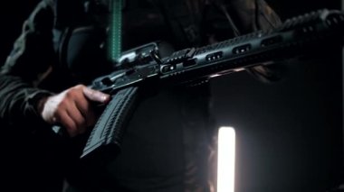 Siyah arka plandaki bir adam makineli tüfeği savaş pozisyonuna getiriyor.