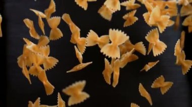Farfalle makarnası havada uçuşuyor ve siyah arka planda asılı duruyor.