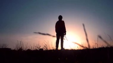 Gün batımında dizlerinin üstüne çöken bir adamın silueti.