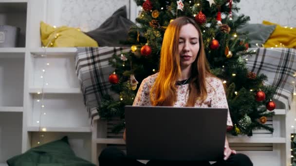 Mooi Meisje Werken Een Laptop Onder Een Kerstboom Terwijl Zitten — Stockvideo