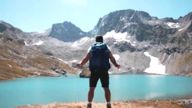 Beyaz tişörtlü bir gezgin, bir dağın tepesindeki dağ gölünün yakınlarında çaresizce bir jest yapıyor.