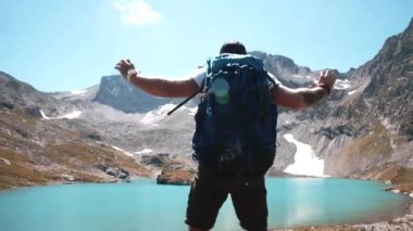 Sakallı gezgin dağın tepesinde bir dağ gölünün yanında duruyor ve zafer kazanıyor.