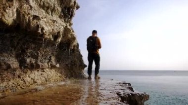 Gezgin şelalenin yanındaki bir kayanın üzerinde duruyor ve denize bakıyor.