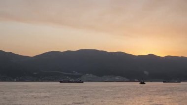 Gemiler ve tepelerle birlikte körfezin üzerinde güneş doğuyor. Zaman Uygulaması