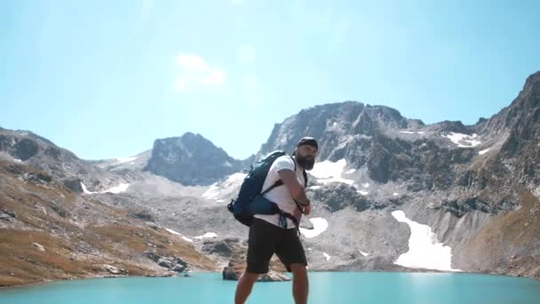 一个留着胡子的徒步旅行者站在靠近高山湖畔的山顶上 兴高采烈地胜利了 — 图库视频影像