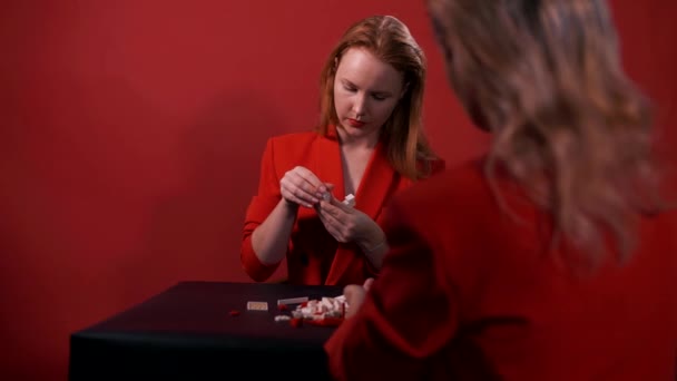 美しい若い女の子はお互いに向かいのテーブルに座って 赤い背景にコンストラクターを収集します — ストック動画