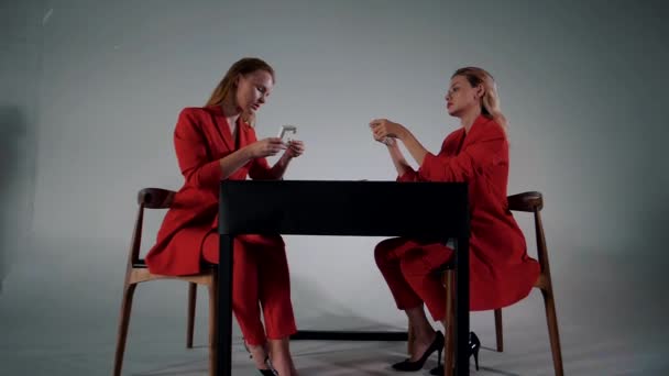 两个穿着红衣服的年轻漂亮的姑娘坐在对面的一张桌子上 收集着一个建设者 — 图库视频影像